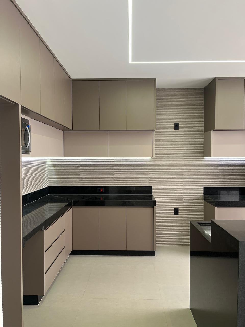 Cozinha com móveis planejados em tons neutros, bancada preta e iluminação embutida
